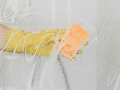 Cleaner with yellow rubber gloves scrubbing a shower door.